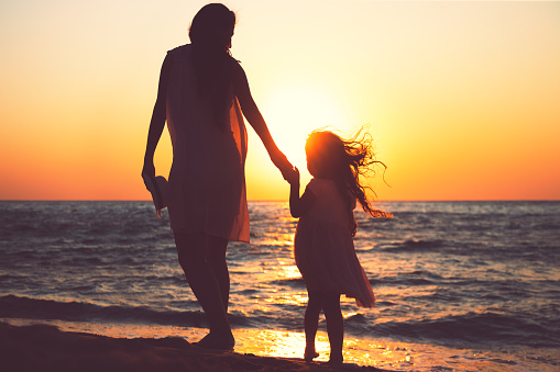 Mother and daughter playing together on the sea beach at sunset.