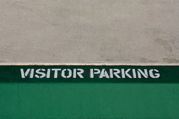 Stenciled letters on green curb indicate where visitors may park. Focus on lettering.