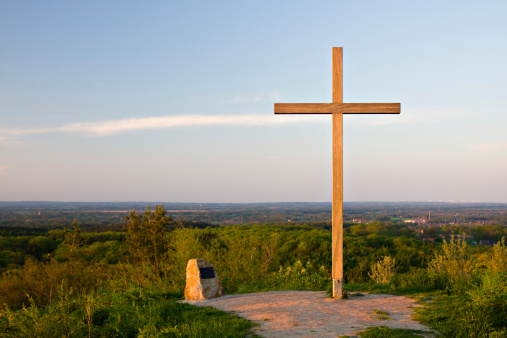 Wooden cross stands on a hill on a background of sky