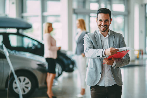 Successful businessman in a car dealership - sale of vehicles to customers Successful happy businessman in a car dealership - sale of vehicles to customers salesman stock pictures, royalty-free photos & images