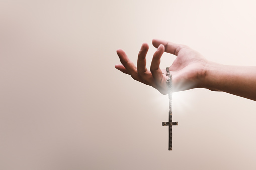 Praying hands hold a crucifix or cross of metal necklace with faith in religion and belief in God on confession background. Power of hope or love and devotion.