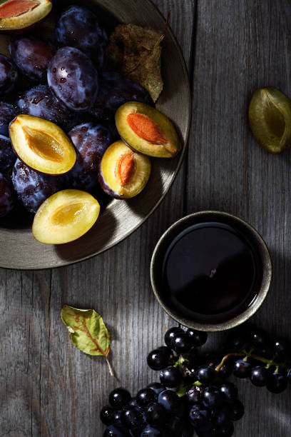 fresh ripe plum in a plate and grapes on an old wooden table. dark background. top view. - plum fruit organic food and drink imagens e fotografias de stock