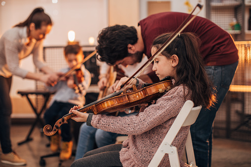 Group of people, teachers and children in music school, learning to play music instruments together.