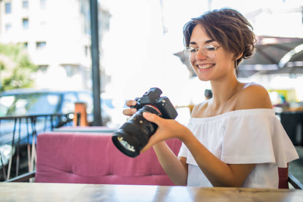 istock Young smiling woman holds camera in her hands and looking at camera while sitting at the table in outdoor cafe 1172437744