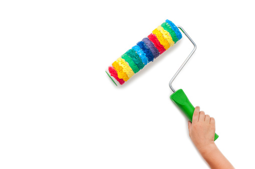 Kids hand holding rainbow paint roller isolated on white background with blank space for text