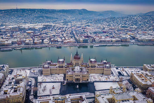 Budapest, Hungary - Aerial view of the snowy Parliament of Hungary at winter time with River Danube and Fisherman's Bastion at background