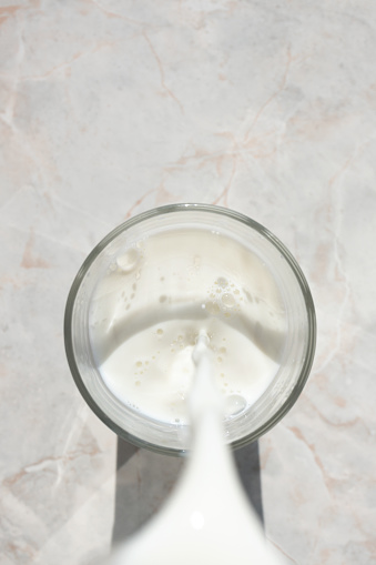 Flowing milk. Close-up of milk stream pouring into glass. Top view, light stone background. Vegan milk, coconut milk or rice milk