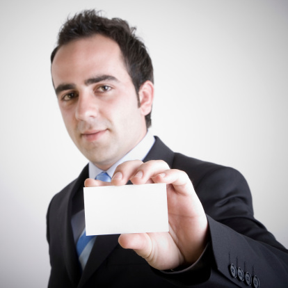 Young businessman showing his business card. Shallow depth of field - focus on fingers and card. Empty space for message