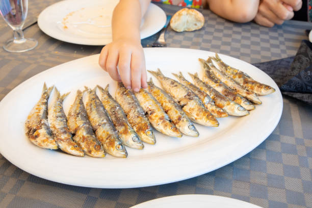 hand of little child taking sardines in a row cooked in a big white dish stock photo