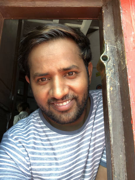 istock Image of young happy smiling handsome Indian man looking through a lighthouse window, Kollam, Kerala, India, looking at camera and posing, wearing T-shirt, sunny day 1172464179