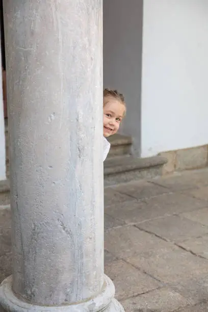 Photo of litlle child peeking behind ancient column