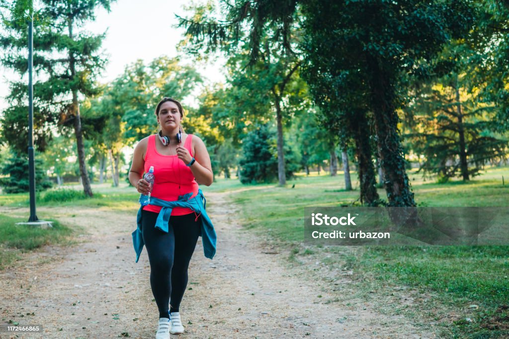 Young overweight woman running Young cute caucasian overweight woman running in a public park. Power Walking Stock Photo
