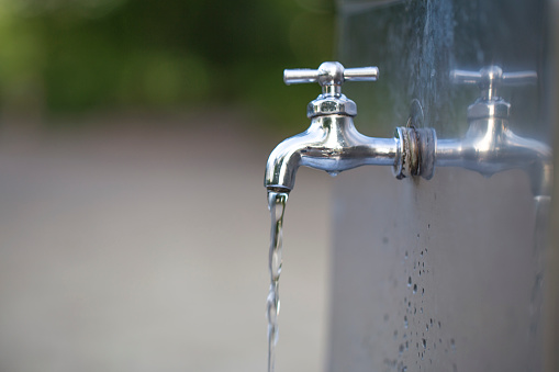 Water tap with water drop outdoor green park background