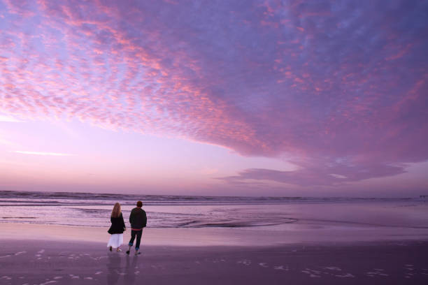 Couple walking on beach at sunrise, enjoying time together. Beautiful cloudy sky reflected on the beach, People relaxing on summer  vacation.  Jacksonville, Florida, USA.