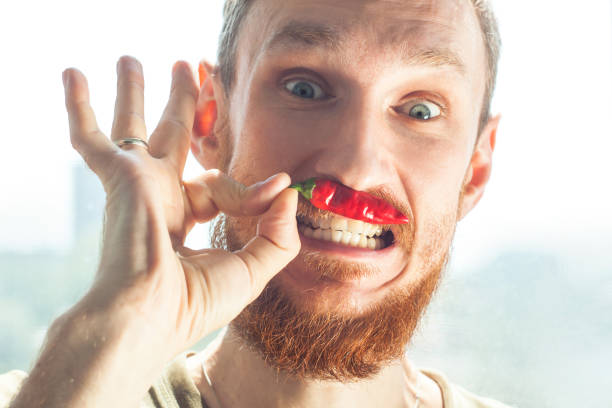 Handsome bearded man bites a red hot chili pepper and smiles.
