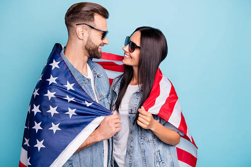 Profile side photo of cheerful married people having eyewear eyeglasses, cover their denim jeans jackets with us flag isolated over blue background