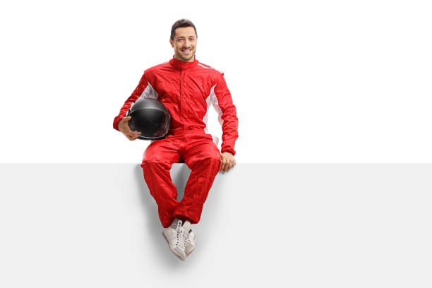 Racer in a red uniform sitting on a panel holding a helmet and smiling Full length portrait of a racer in a red uniform sitting on a panel holding a helmet and smiling isolated on white background race car driver stock pictures, royalty-free photos & images