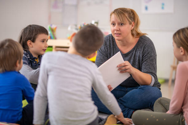 istock Female teacher reading book to her students 1172490511