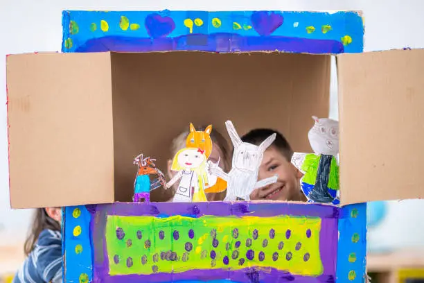 Children playing with paper puppets and painted carton in the classroom.