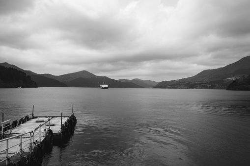 Black and white of the jetty and the lake grey skies thou clam water, watching the ferry arrive in the mountains of Japan