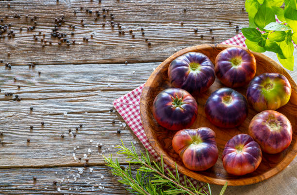 Blue black tomatoes with basil and rosemary on wooden board