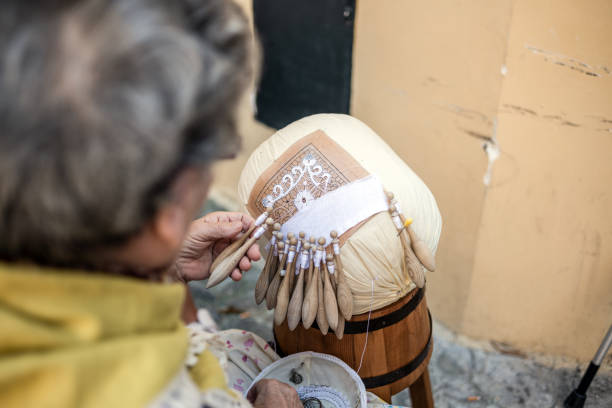 Elderly woman working on a "Merletto a tombolo" (Bobbin lace) in the street in front of her house in Offida Offida, Italy - August 19, 2019: An elderly woman working on a "Merletto a tombolo" (Bobbin lace) in the street in front of her house lacemaking photos stock pictures, royalty-free photos & images