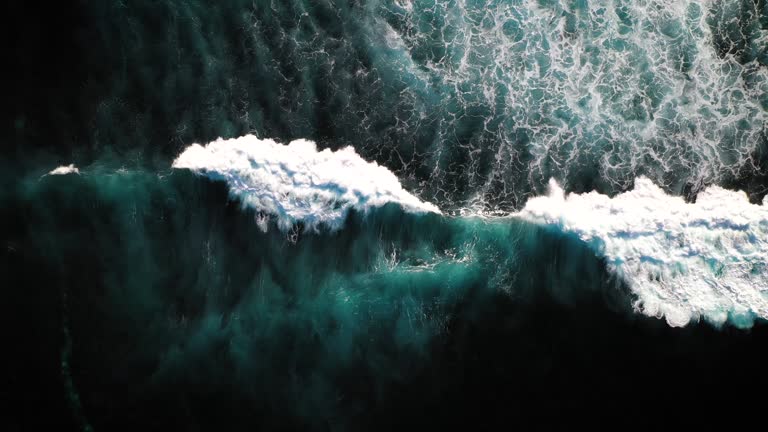 Aerial view of breaking surf in Bali, Indonesia, captured by hovering drone. The powerful waves of Bali and Lembongan is a well known hot spot amongst surfers and attracts many tourists as well. Ocean, secluded beaches and sea cliffs of Nusa Lembongang Island. 4k drone shot, directly from above moving over coral reef break.