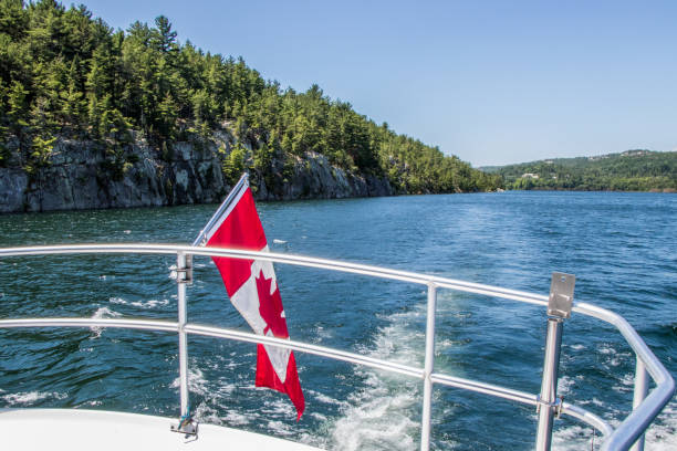 Canadian flag and Baie Fine, Killarney, Ontario, Canada Canadian flag on the back of a boat travelling down a narrow fjord in the North Channel of Killarney, Ontario killarney lake stock pictures, royalty-free photos & images