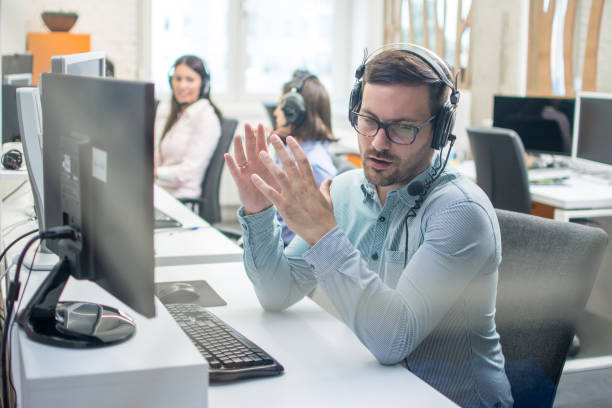 Young handsome male technical support agent trying to explain something to a client while using hands-free headset at call center Young handsome male technical support agent trying to explain something to a client while using hands-free headset at call center dispatcher stock pictures, royalty-free photos & images