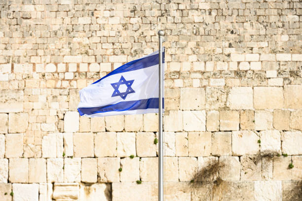 vista de cerca de la bandera israelí ondeando frente al muro de las lamentaciones (muro de las lamentaciones) en jerusalén, israel. la bandera de israel se puede ver en todo el país, y es un símbolo de alegría y sueños. - mount of olives fotografías e imágenes de stock
