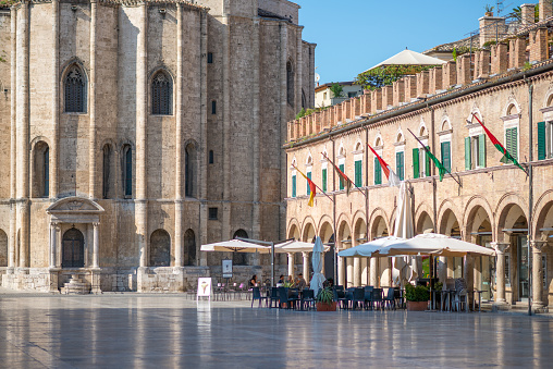 Ascoli Piceno, Italy - August 19, 2019: A view of Piazza del Popolo square with some café tables and the Chiesa di San Francesco basilica church