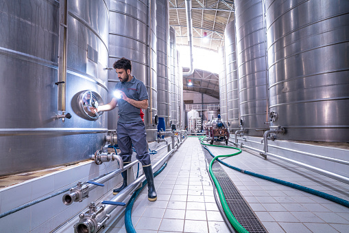 Cellar worker closing wine fermenting tank with a light stainless steel deposit