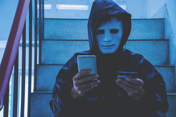 Anonymous computer hacker in white mask and hoodie, Hacker holding credit card and using smartphone. Cyber crime concept, Data thief, internet attack, darknet and cyber security concept. hacker informático anónimo en máscara blanca y sudadera con capucha, hacker sosteniendo tarjeta de crédito y usando teléfono inteligente. concepto de delito cibernético, ladrón de datos, ataque a internet, darknet y concepto de seguridad cibernétic