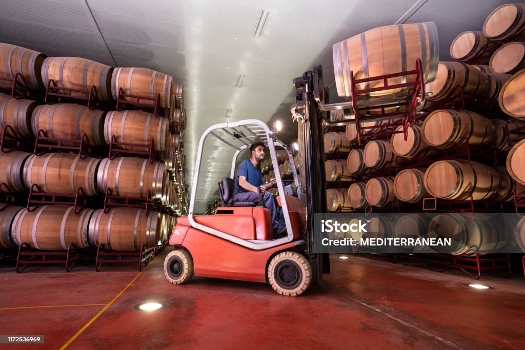Barrel winery pallet truck jack forklift Oak Barrel winery pallet truck jack forklift young beard worker man in cellar Wine Stock Photo
