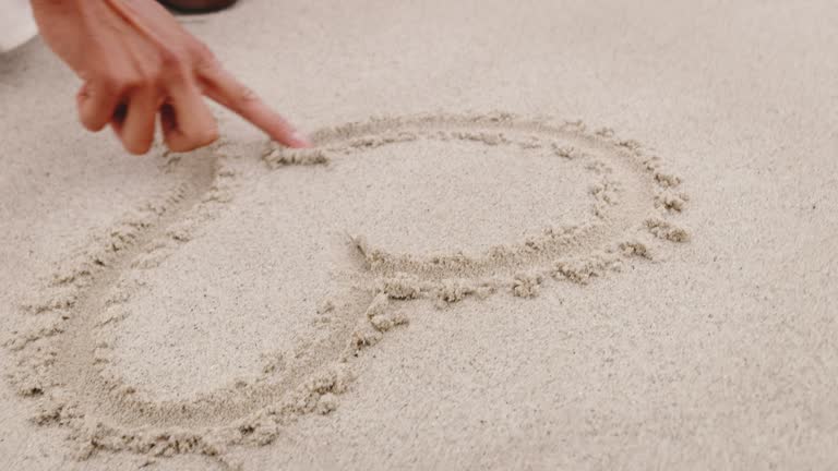 Woman drawing heart shape on sand with finger