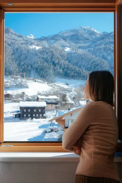Happy woman at balcony looking into houses in Zillertal valley in Tyrol in Austria in winter in Alps. Alpine mountains with snow in Mayrhofen