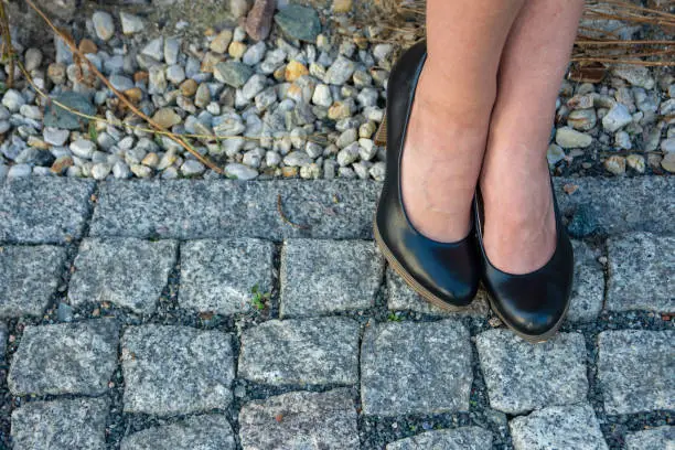 Feet of a woman wearing elegant traditional black court shoes on old cobblestones in a close up view to the side