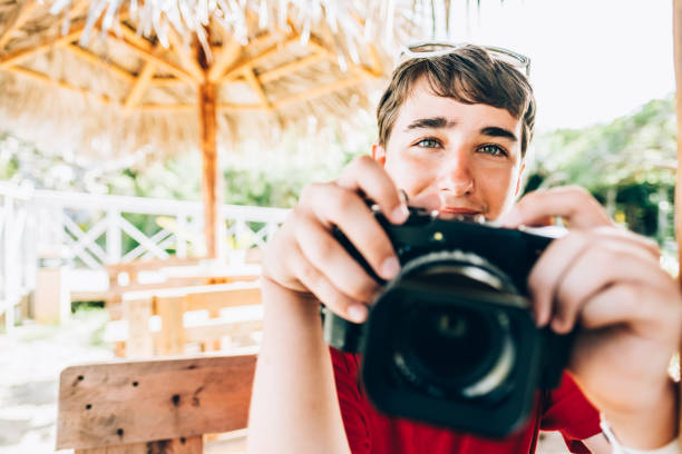 Teenage boy  at cabana at summer resort, using retro digital camera. He is enjoying summer vacation in Caribbean.