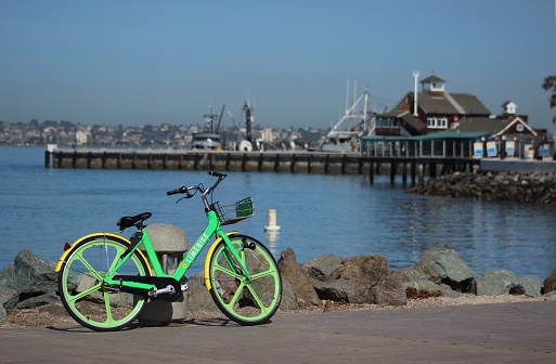 A dockless Limebike bicycle is parked in downtown San Diego, ready to be rented. Pretty view of the marina in the background.