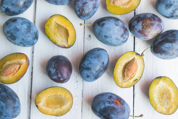 istock Fresh and ripped delicious plums on old white wooden table. High angle view 1172549574
