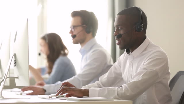 Focused african call center agent wear wireless headset consulting customer