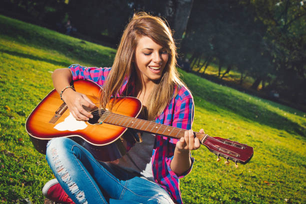 istock Woman sitting on grass and playing guitar 1172555616