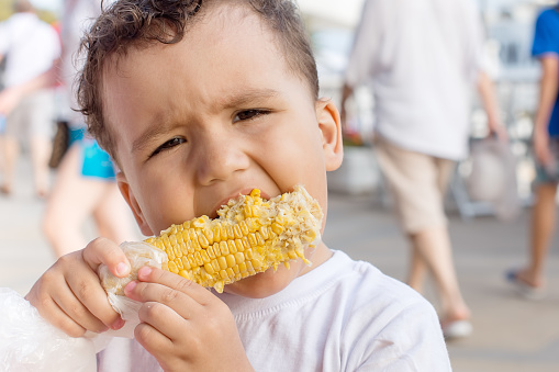 Baby boy eats cob fresh boiled corn in the Park on a summer day