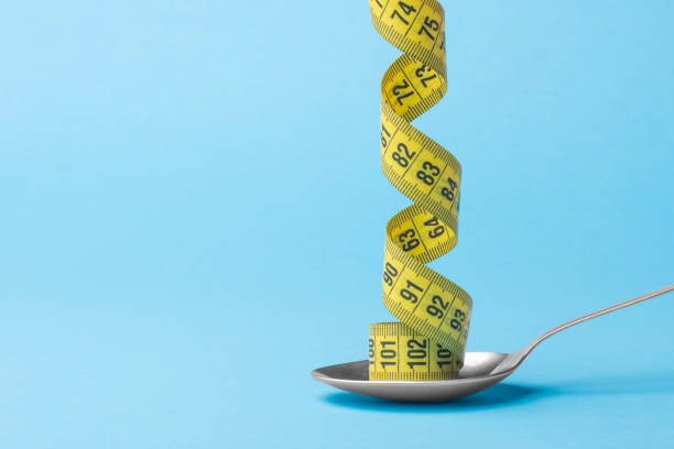 Measuring tape on a tablespoon, minimum creative concept-diet healthy lifestyle. Measuring tape on a tablespoon, minimum creative concept-diet healthy lifestyle. eating disorder stock pictures, royalty-free photos & images