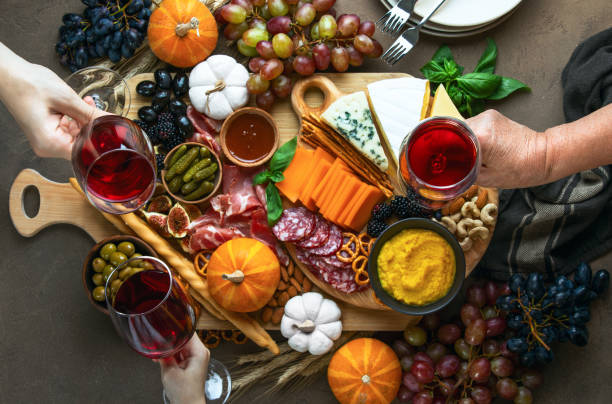 Fall party charcuterie board, view from above Fall holidays party table with friends hands holding wine glasses above charcuterie board, top down view prosciutto brie stock pictures, royalty-free photos & images