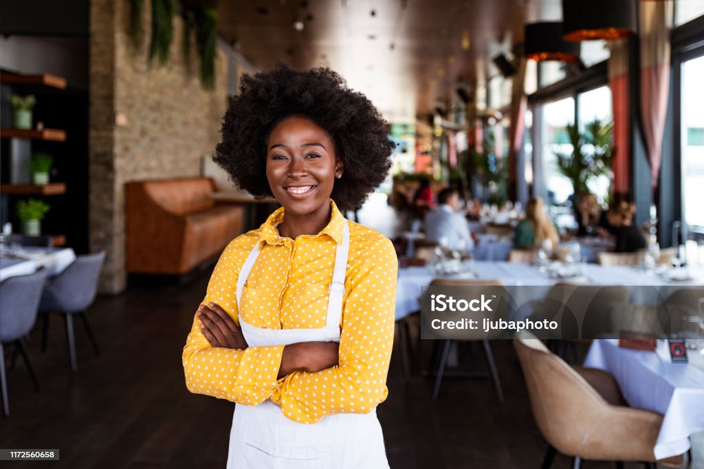 Say hello to the new boss! Portrait of positive African american young woman working professional confectioner in own coffee shop, looking at camera with toothy smile. Restaurant Stock Photo
