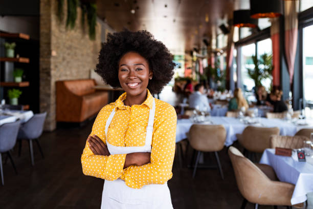 Say hello to the new boss! Portrait of positive African american young woman working professional confectioner in own coffee shop, looking at camera with toothy smile. waiter photos stock pictures, royalty-free photos & images