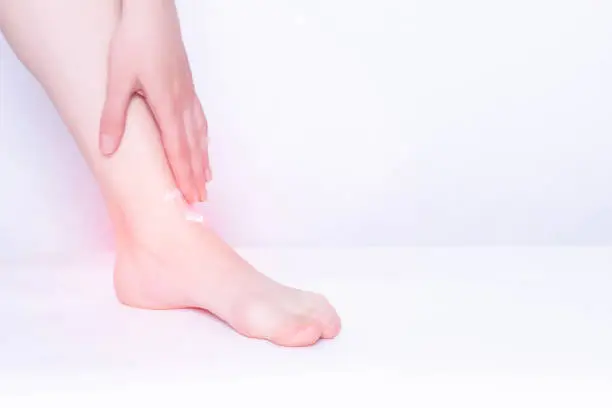 Girl smears medical ointment ankle on a white background, treatment of synovitis and bursitis, inflammation, copy space, osteoarthritis, rheumatoid