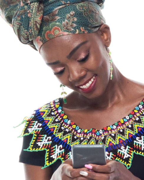 headshot / profile view of 20-29 years old african ethnicity / african-american ethnicity young women / female in front of white background wearing headscarf / dress / traditional clothing who is smiling / happy / cheerful and holding mobile phone - one young woman only only young women one woman only 20 25 years imagens e fotografias de stock
