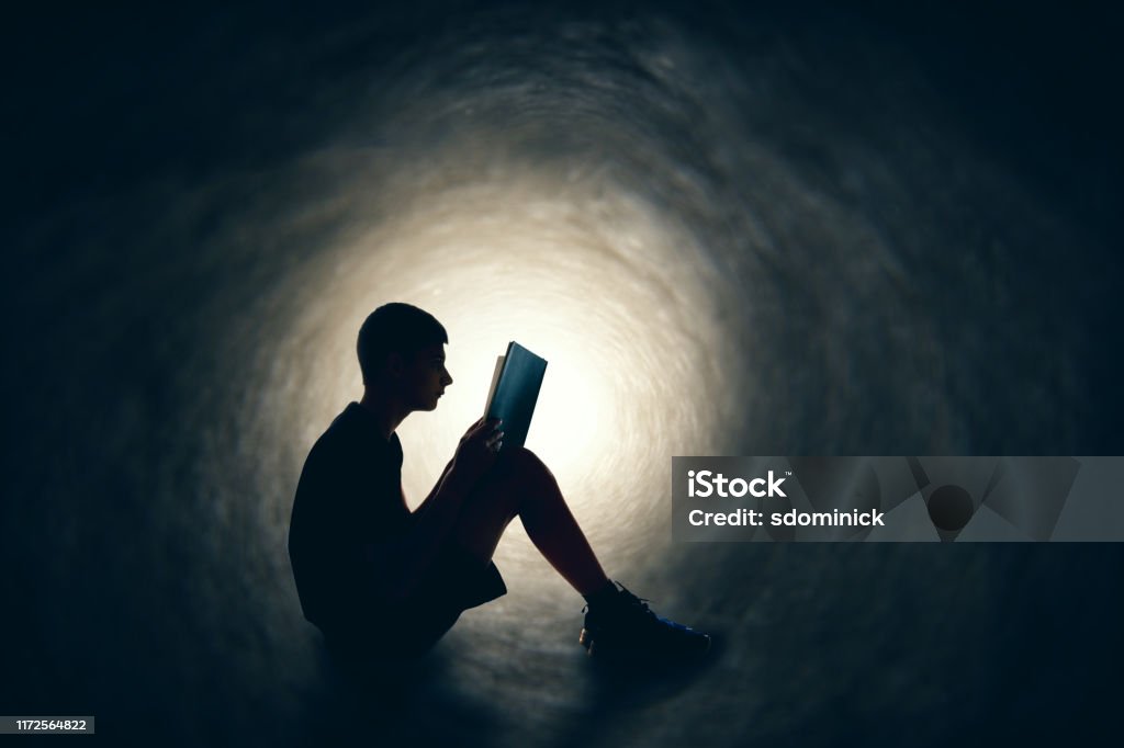Adventures in Reading A silhouette of a teen boy reading a book is whisked away to somewhere else as sits and reads. Book Stock Photo